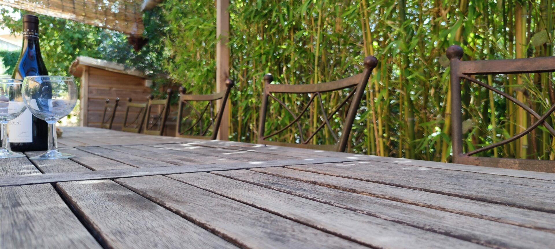 Grande table de jardin en bois et chaises en fer forgé sous une tonnelle au Pradet, gîte de groupe Var.