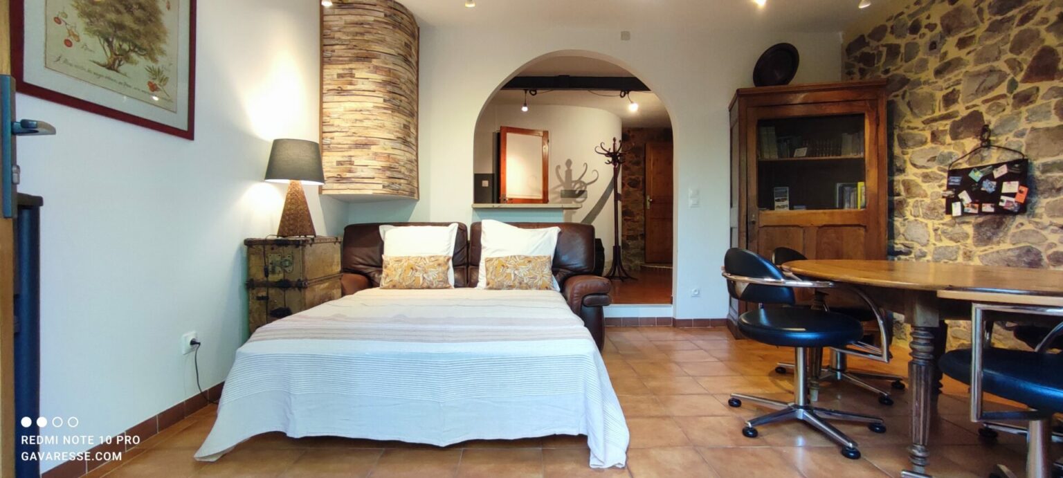 Canapé clic-clac en cuir marron déplié, offrant des couchages supplémentaires dans l'espace salon-salle à manger d'un gîte de vacances au Pradet, avec table en bois et mur en pierre apparente.