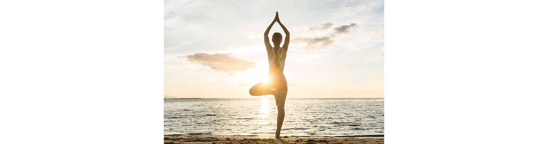 Silhouette of a woman practicing the yoga tree pose on the beach of Le Pradet at sunrise.
